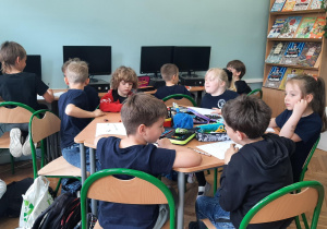 Dzieci pracują przy stolikach rysując strój łowicki