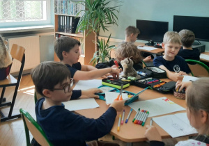 Uczniowie pracują przy stoliku tworząc pracę plastyczną
