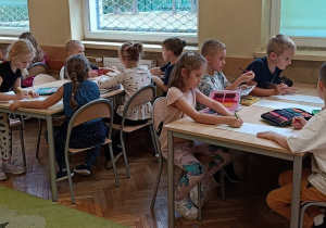 Uczniowie pracują przy stolikach wykonując zadanie plastyczne