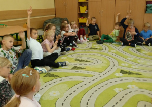 Uczniowie siedzą w kole na dywanie