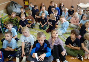 Uczniowie siedzą na dywanie