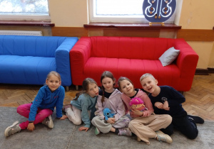 Uczniowie siedzą na dywanie przy sofach