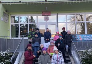 Uczniowie z nauczycielkami stoją na schodach przed szkołą
