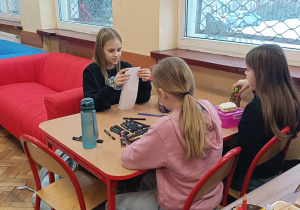 Dziewczynki tworzą pracę plastyczną przy stoliku