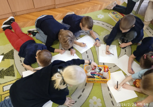 Uczniowie siedzą na dywanie