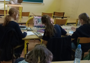 Uczennice siedzą w ławkach i malują