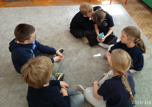 Uczniowie siedzą w kole na dywanie