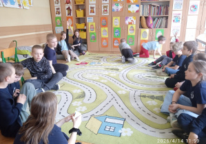 Uczniowie siedzą w kole na dywanie