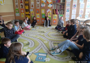 Uczniowie siedzą w kole na dywanie
