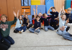 Uczniowie podnoszą rękę siedząc na dywanie